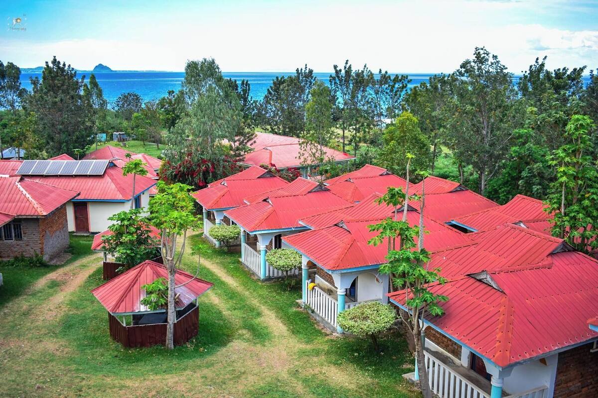 Un resort con varias cabañas de techo rojo, algunas con paneles solares, rodeado de exuberante vegetación y vistas al océano.