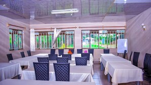 A conference room with multiple tables and chairs, large windows with curtains, and a whiteboard.
