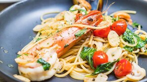 A plate of pasta with shrimp, cherry tomatoes, and greens.