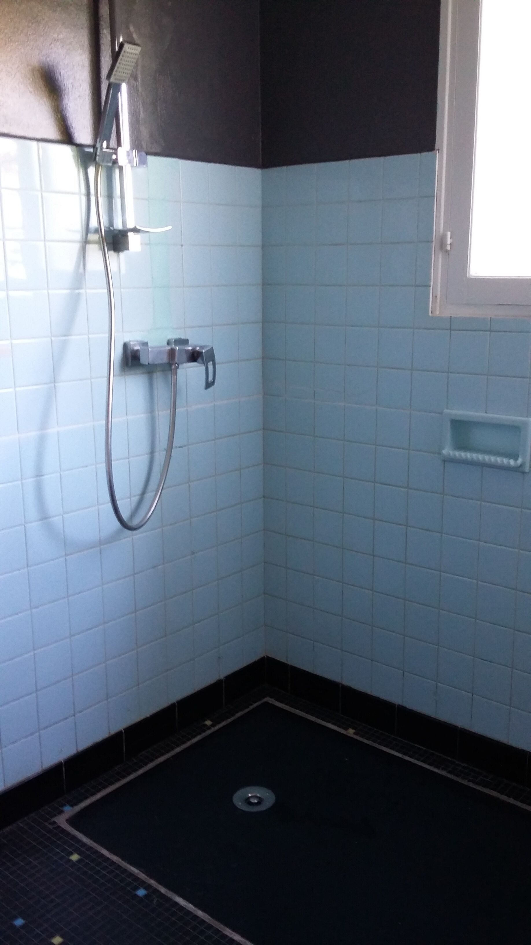 Ein Badezimmer mit blauen Fliesen, einer Dusche und einem Fenster.