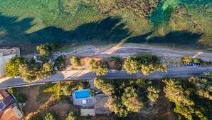 An aerial view of a coastal property with a swimming pool, a road, and surrounding greenery. - Deja Blue Beach Pool House by Estia (Corfu)