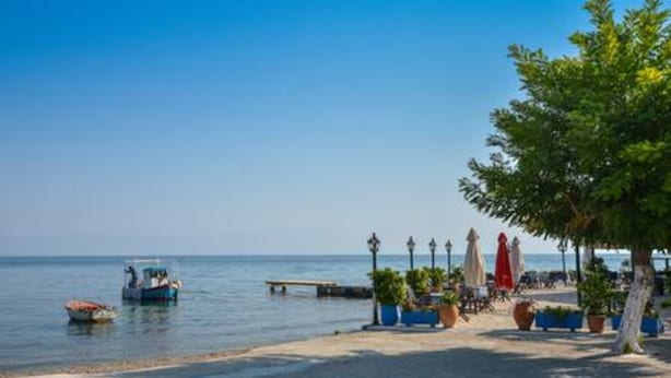 A beachside scene with a boat, a pier, and a row of potted plants and umbrellas. - Deja Blue Beach Pool House by Estia (Corfu)