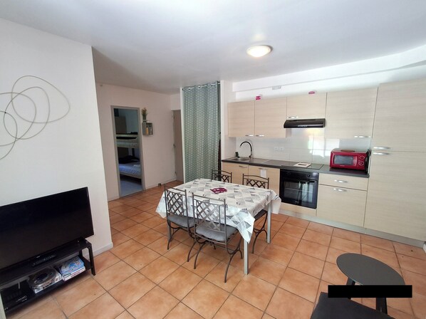 A compact living space with a dining area, kitchenette, and a TV on a stand.