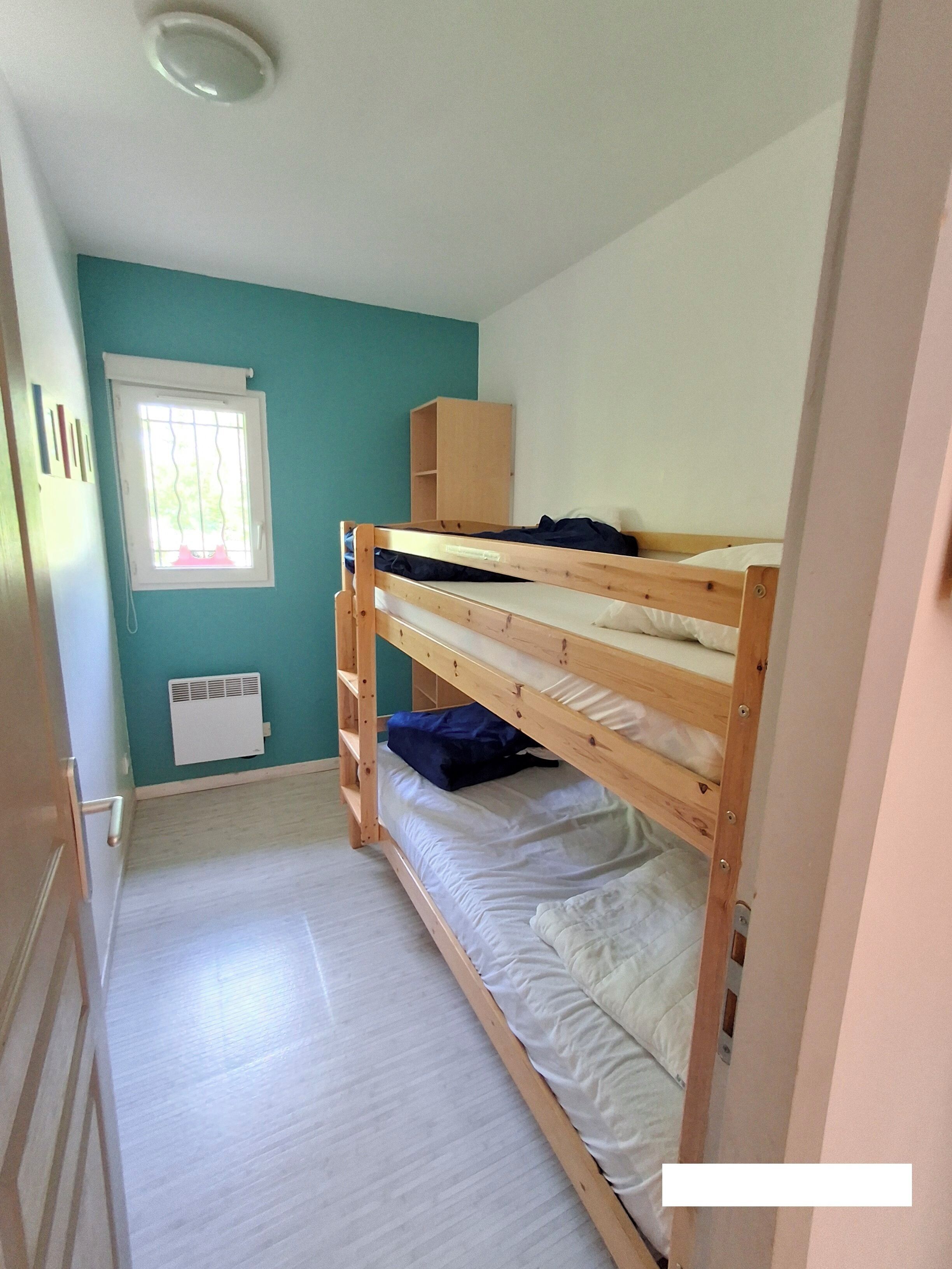 A room with a bunk bed, a window with blinds, a radiator, and a door.