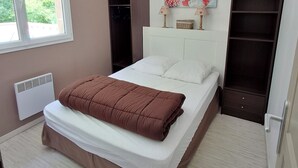 Un dormitorio con cama, ventana, armario y estante con objetos decorativos.
