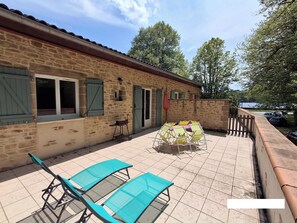 A stone building with a tiled patio, outdoor seating, and a view of a lake.