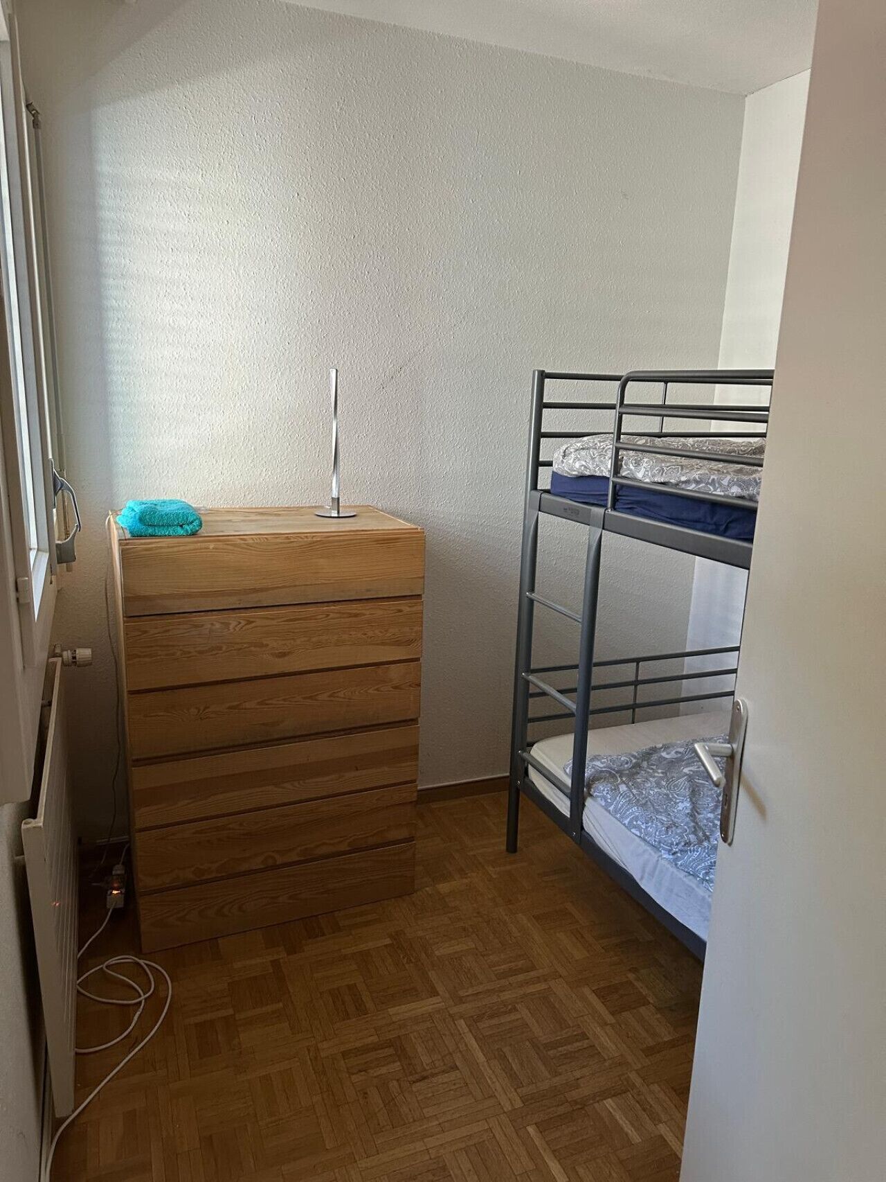 A small room with a bunk bed, a wooden dresser, and a radiator.