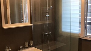 Un baño moderno con ducha de vidrio, tocador con lavabo y espejo con iluminación superior.