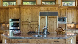 A kitchen with wooden cabinets, stainless steel appliances, a granite countertop, and a large island with a sink. - Maison de Neige Breathtaking Mountain Stay for 8 w/ Hot Tub (Vail)