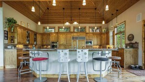 A spacious kitchen with wooden cabinets, a central island with bar stools, and pendant lighting. - Maison de Neige Breathtaking Mountain Stay for 8 w/ Hot Tub (Vail)