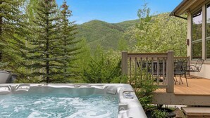 A hot tub with a wooden deck and chairs, surrounded by trees and a mountain view. - Maison de Neige Breathtaking Mountain Stay for 8 w/ Hot Tub (Vail)