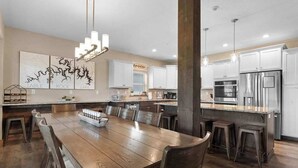 Una cocina moderna con armarios blancos, electrodomésticos de acero inoxidable y una mesa de comedor de madera con taburetes de bar.