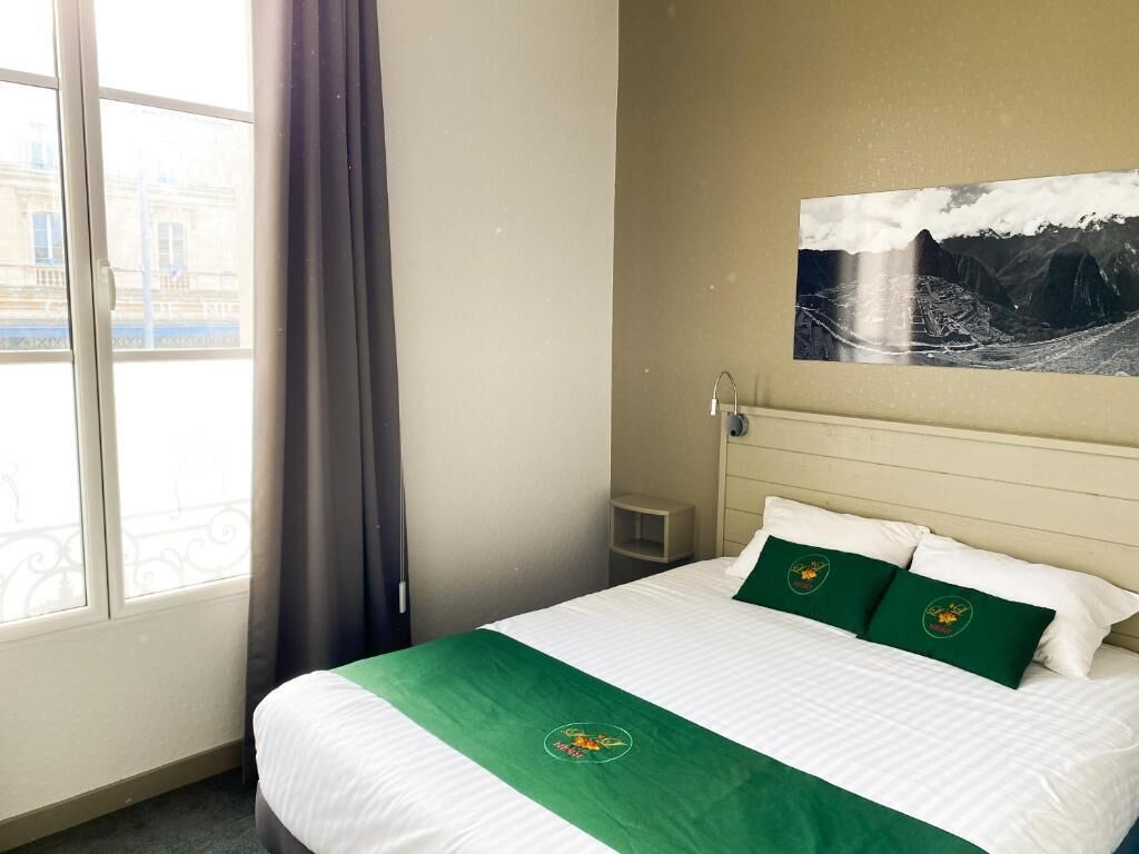 Een hotelkamer met een bed, een raam en een schilderij aan de muur.