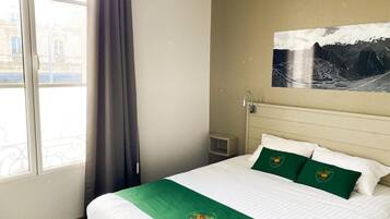 Een hotelkamer met een bed, een raam en een schilderij aan de muur.