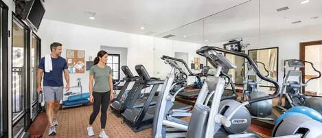 A gym with treadmills, ellipticals, and a mirrored wall.