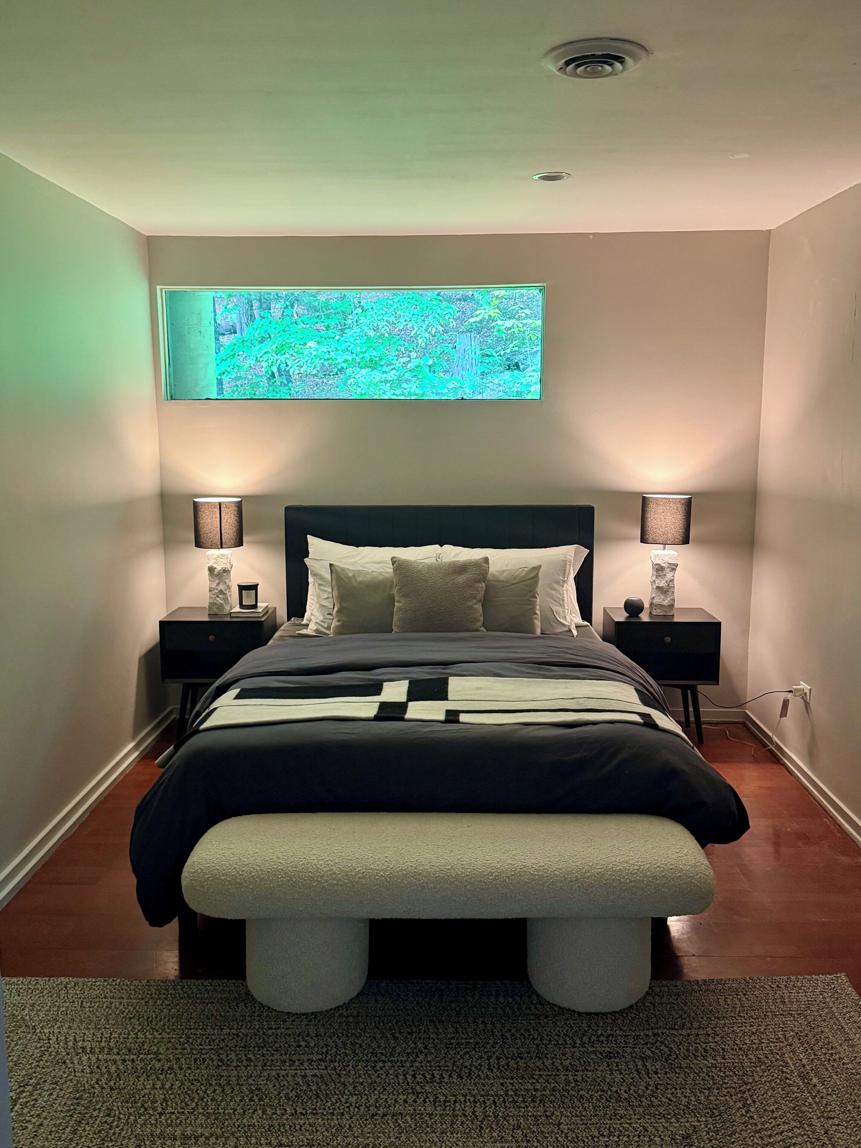 Ein modernes Schlafzimmer mit einem Bett, zwei Nachttischen, einer Bank, einem Wand-Fernseher und einer Deckenleuchte.