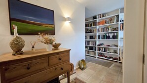 A room with a wooden dresser, a painting of a landscape, a bookshelf filled with books and decorative items, and a patterned rug on the floor. - Toca do Fradinho - Pera 3 7Km da Praia (Silves)