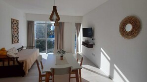 A modern living room with a dining table, chairs, a sofa, a TV, and a large window.