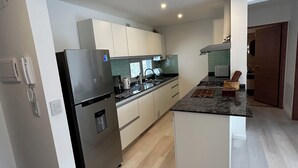 A modern kitchen with white cabinets, a stainless steel refrigerator, and a granite countertop.