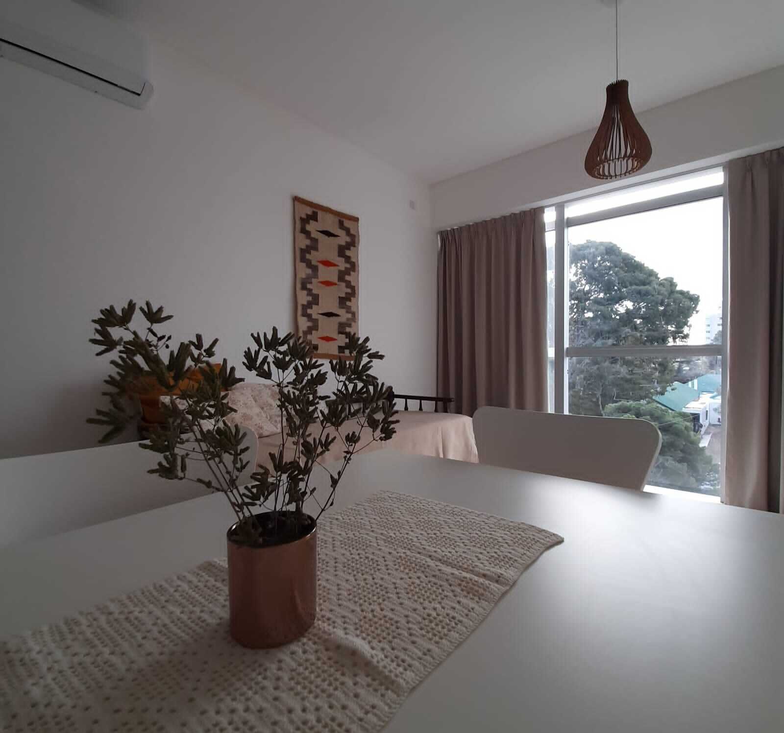 Ein modernes Schlafzimmer mit einem großen Bett, einer Topfpflanze, einer Pendelleuchte, einem Fenster mit Vorhängen und einer wandmontierten Klimaanlage.