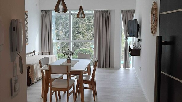 A spacious dining area with a wooden table and chairs, large windows with curtains, and pendant lights.