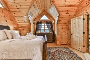 Quarto de cabana de tronco com cama, cômoda e uma janela grande.