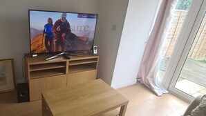 Een woonkamer met een televisie op een houten dressoir, een lijst met foto aan de muur, en een schuifdeur die leidt naar een buitenruimte.