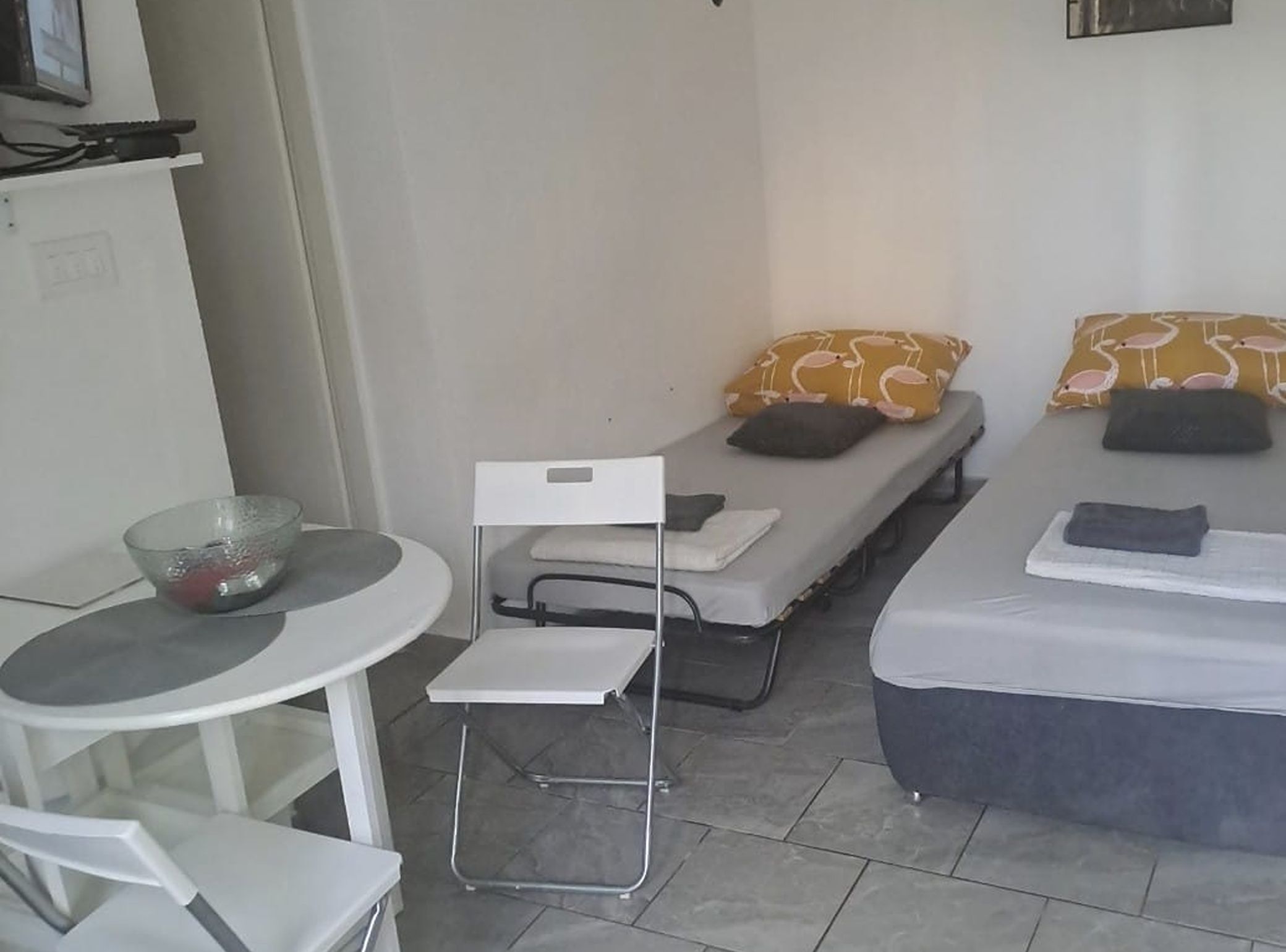 A small, clean room with two single beds, a small table with a bowl, and a chair.