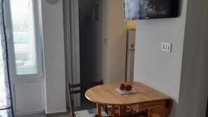 Un coin repas avec une table et des chaises en bois, une horloge au mur et un téléviseur fixé au-dessus de la table.