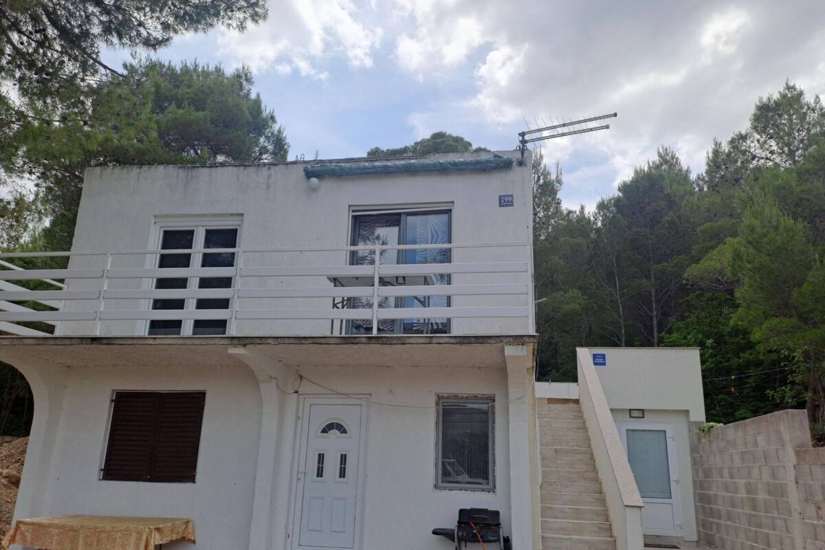 A two-story white building with a balcony, a small table, and a staircase leading to an upper level.