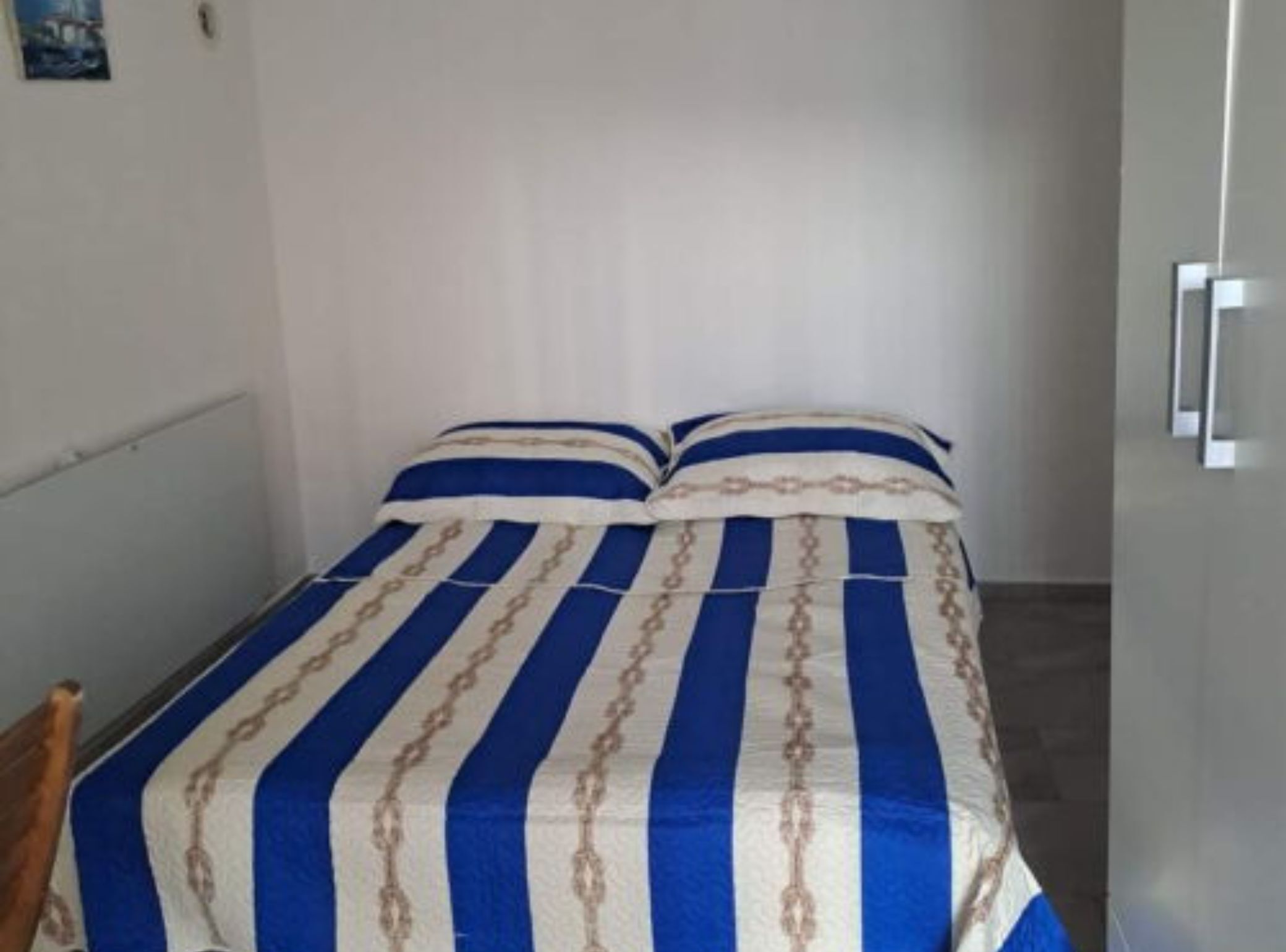 A single bed with a striped bedspread in a room with white walls and a door.