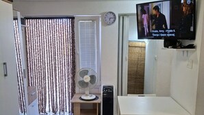 Un espace de vie compact comprenant une télévision, un ventilateur, une horloge et une petite table.