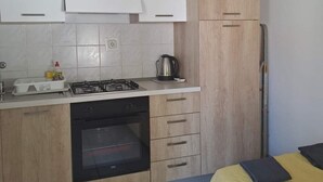 Une cuisine compacte avec des meubles blancs, une cuisinière à gaz, un four et une bouilloire.