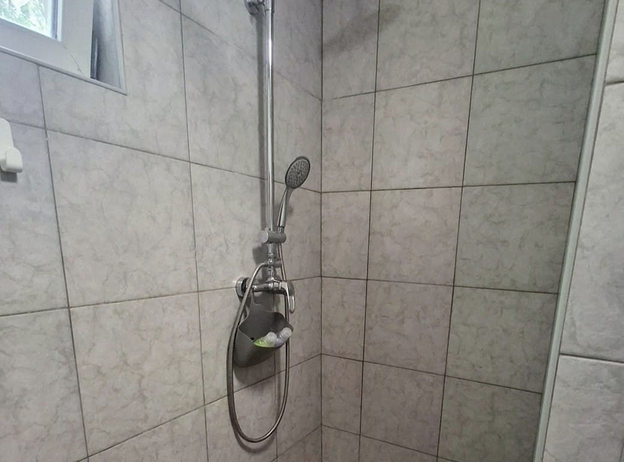 Ducha con cabezal de ducha y manguera de mano, instaladas en una pared de azulejos.