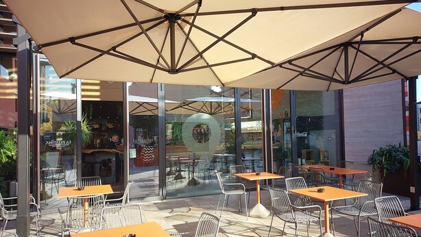 Een terras met tafels en stoelen, grote parasols en glazen etalages.