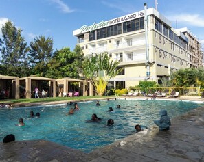 Ein Hotel mit Schwimmbad, umgeben von Liegebereichen und Palmen.
