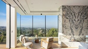A modern living room with a large window, a marble accent wall, and a sofa. - Royal Oak - Exquisite Estate with Infinity Pool & Breathtaking Views (Encino)