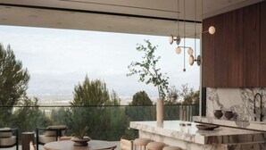 A modern kitchen with a marble countertop, bar stools, and a view of the city. - Royal Oak - Exquisite Estate with Infinity Pool & Breathtaking Views (Encino)