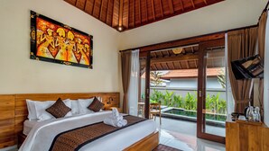 Habitación de hotel con una cama grande, cabecero de madera, un cuadro sobre la cama, un televisor sobre un mueble de madera, y vistas a una piscina y vegetación desde el exterior.