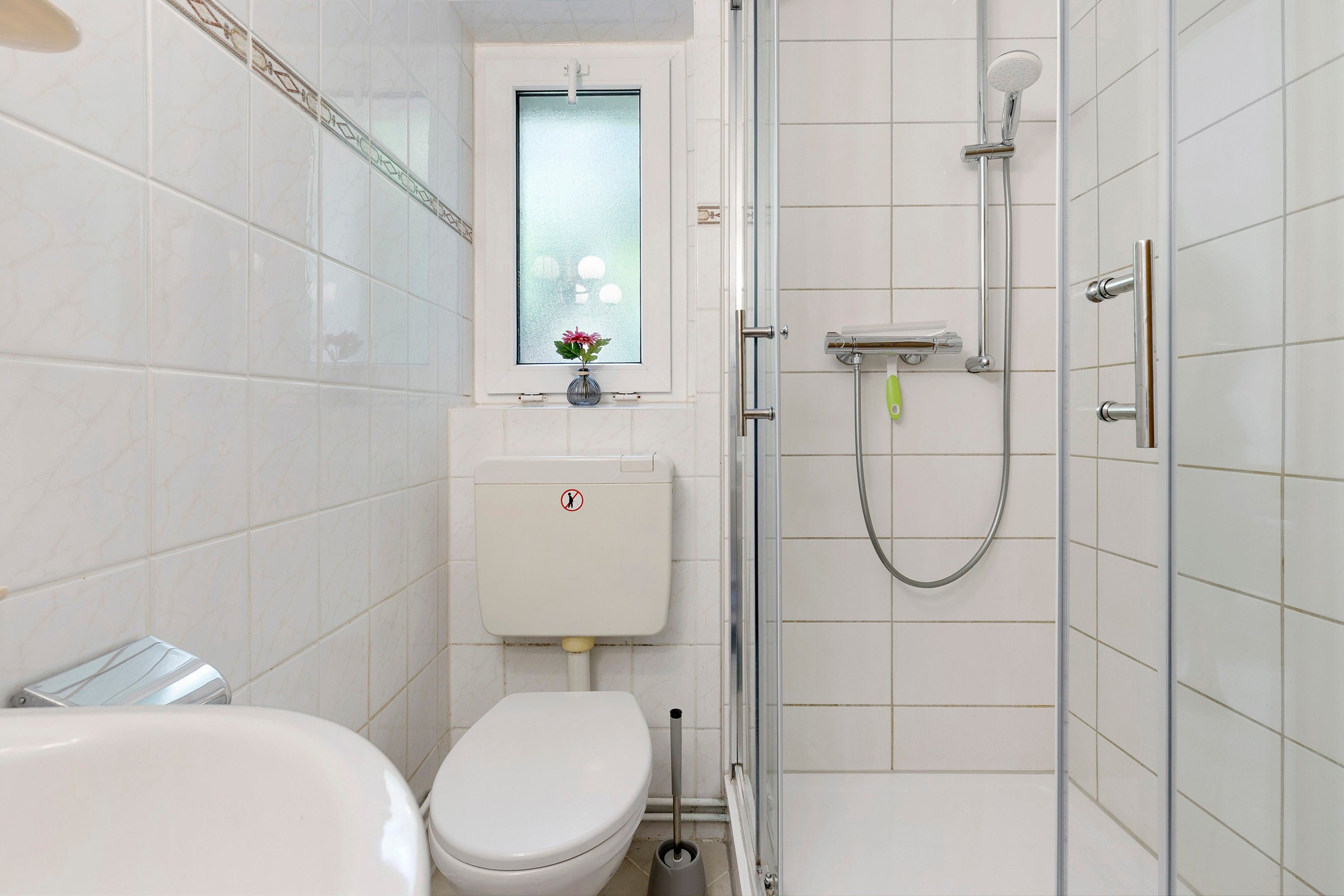 Ein Badezimmer mit Toilette, Dusche und einem Fenster mit Blumenvasen.