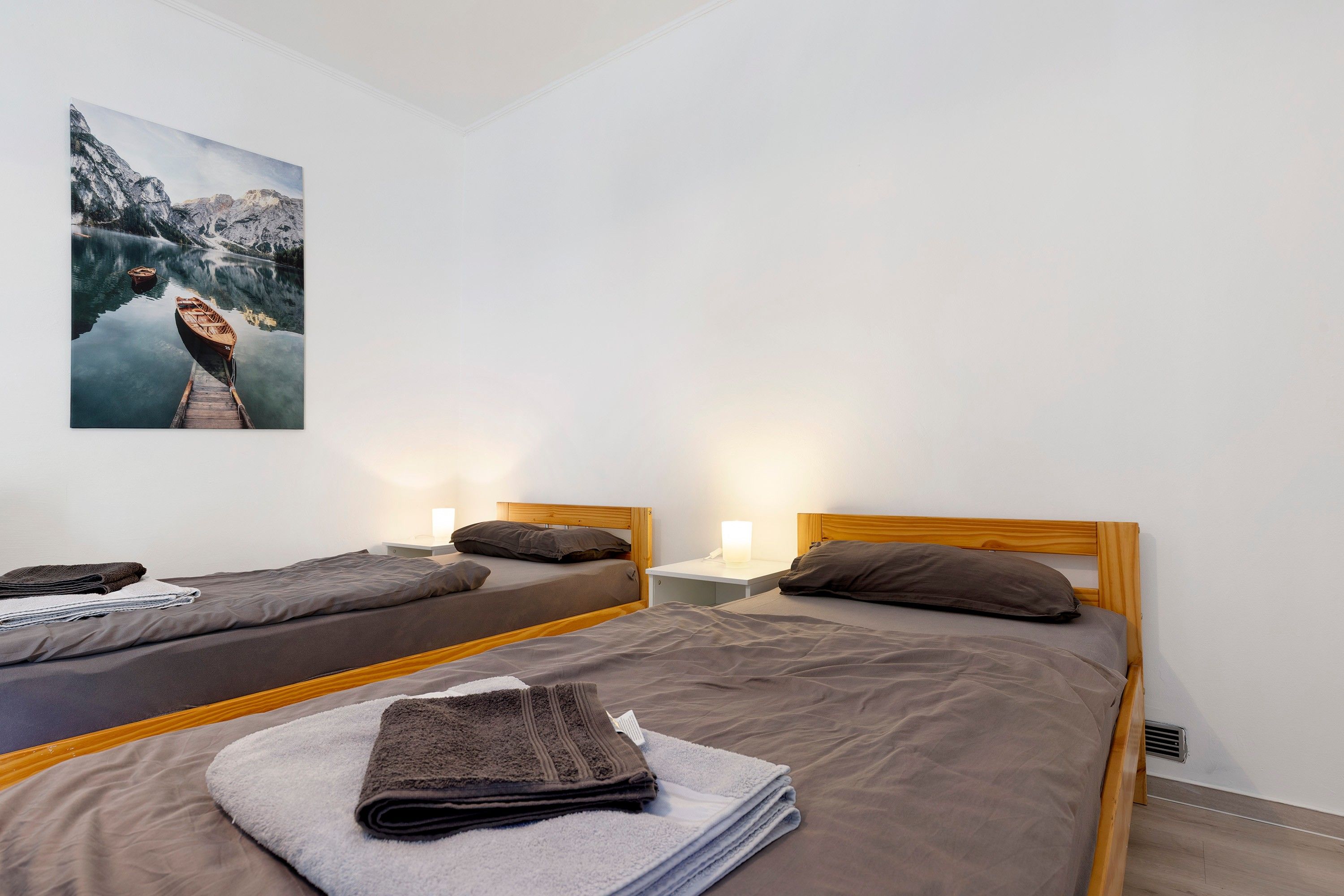 Ein Hotelzimmer mit zwei Betten, einem hölzernen Kopfteil, einem Nachttisch mit Lampe und einem Gemälde einer Berglandschaft.