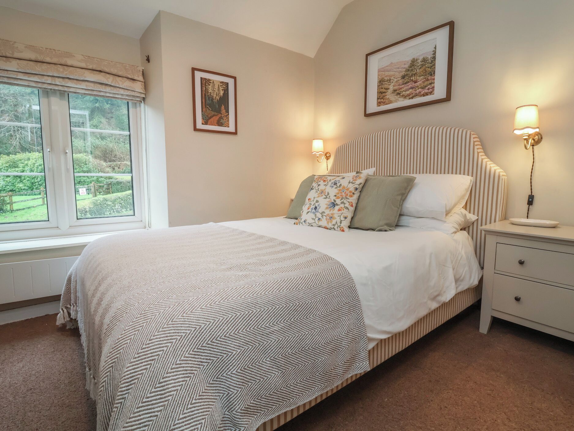 A neatly arranged bedroom with a bed, bedside lamps, a nightstand, and two framed pictures on the wall.