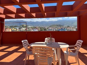 A terrace with a table and chairs, a view of a cityscape, and a red ceiling structure. - Penthouse downtown Puerto de la Cruz (Puerto de la Cruz)