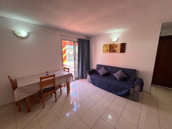 A living room with a sofa, a dining table with chairs, and a sliding glass door leading to an outdoor area.