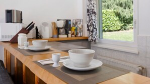 A kitchen with a wooden countertop, white plates, a coffee maker, and a window with a view of greenery.
