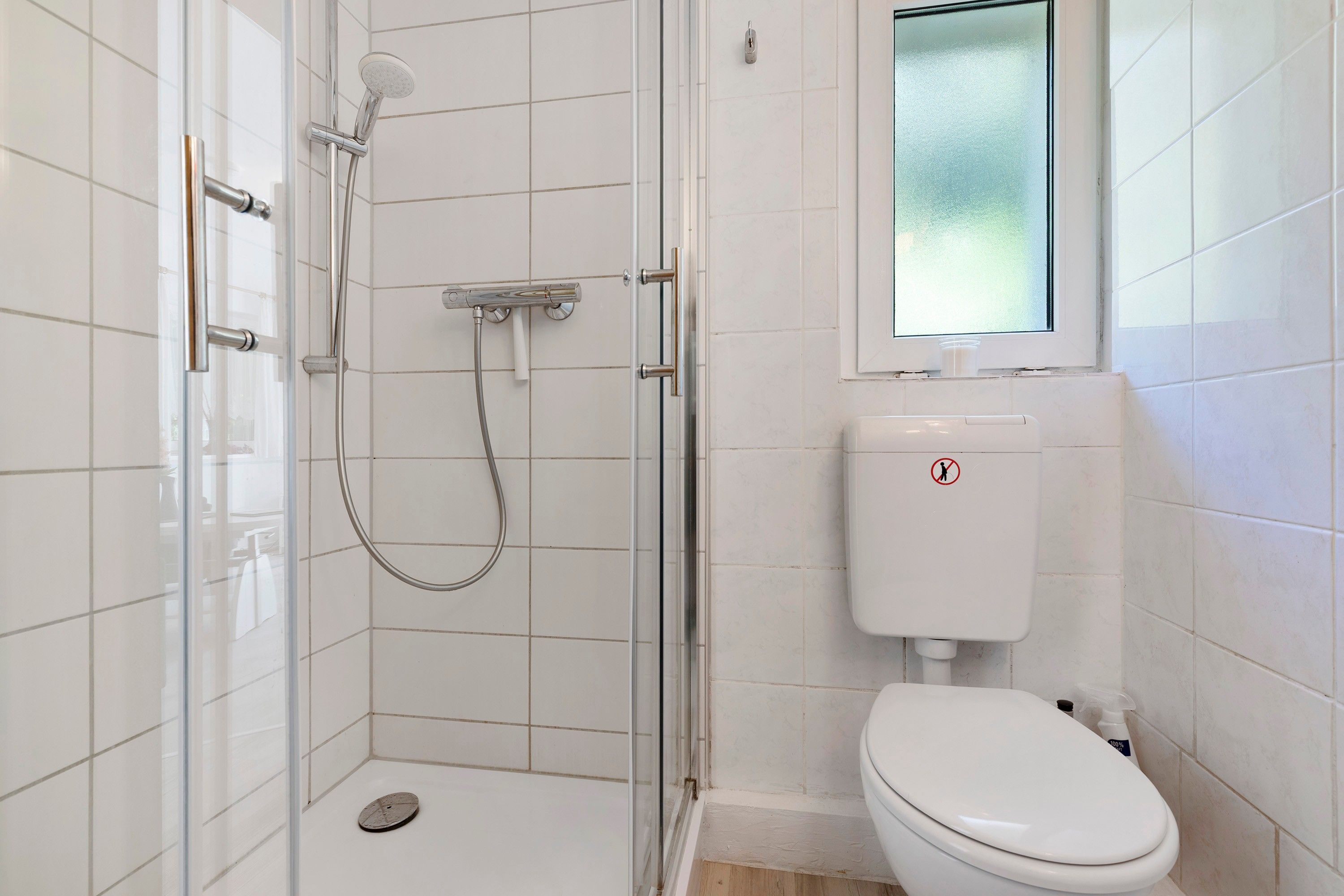 A small, tiled bathroom with a shower, toilet, and a window.