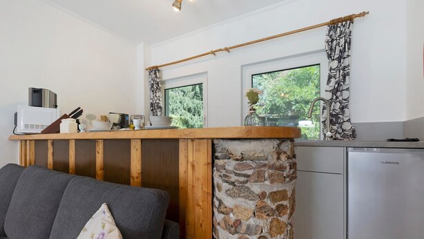 A compact kitchen with a stone column, a wooden counter, and a view of greenery outside.