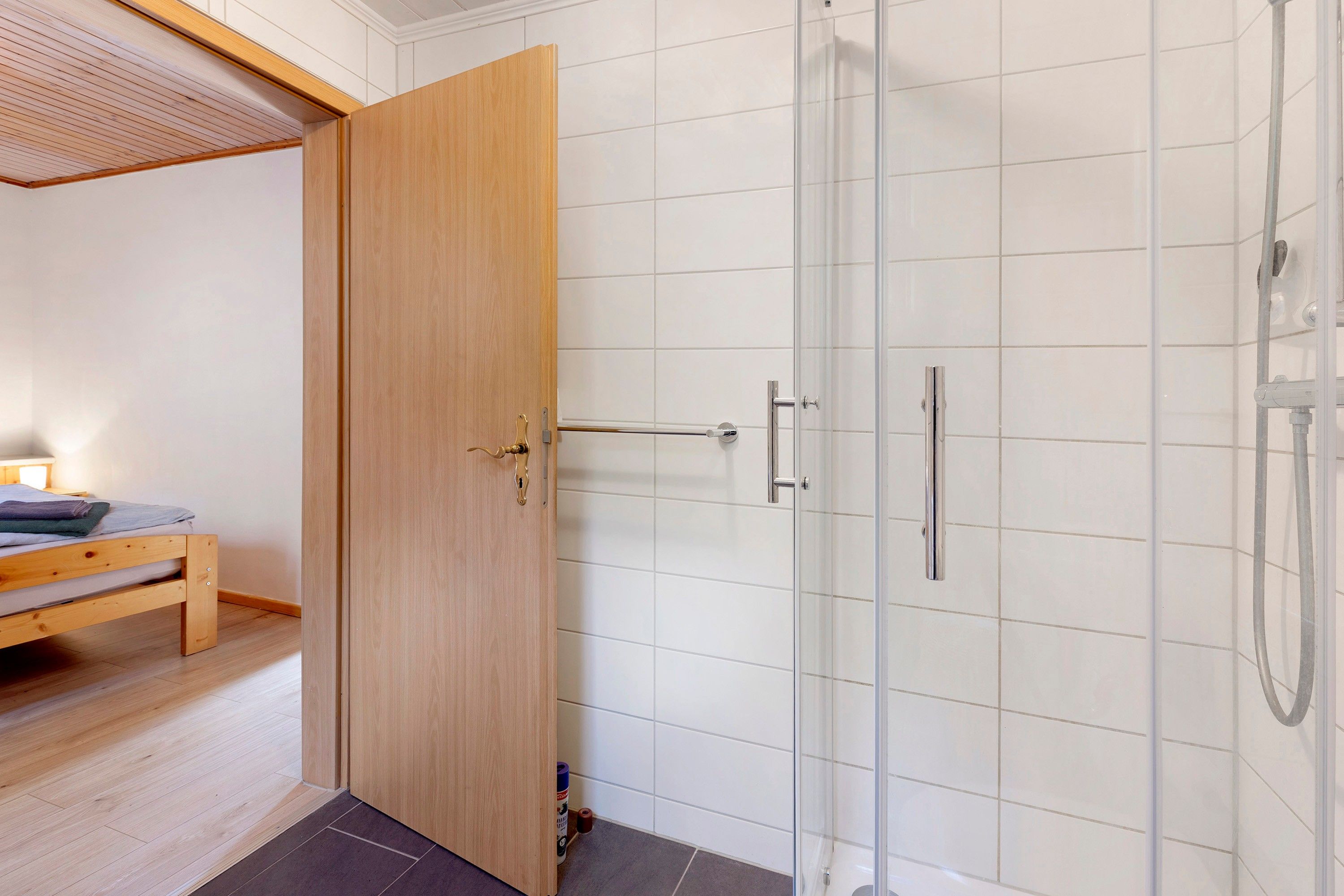 Una habitación con puerta de madera, una cama, un banco y zona de ducha.