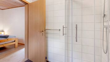 Una habitación con puerta de madera, una cama, un banco y zona de ducha.