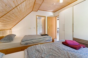 A room with two beds, a wooden ceiling, a mirror, and a wardrobe.